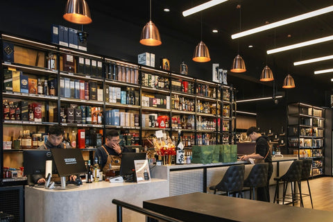 Bar with shelves stocked with bottles, patrons at the bar, and a counter.